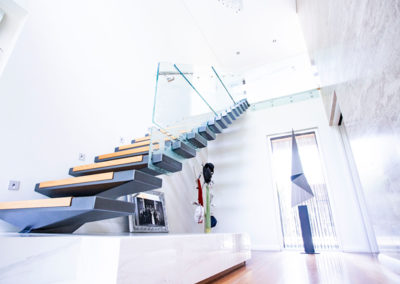 Elegant staircase with a glass railing and white wall, showcasing refined aluminium and sheet metal design