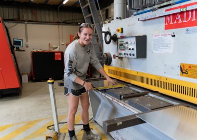 Custom Aluminium employee measuring a metal sheet next to the fabrication machine